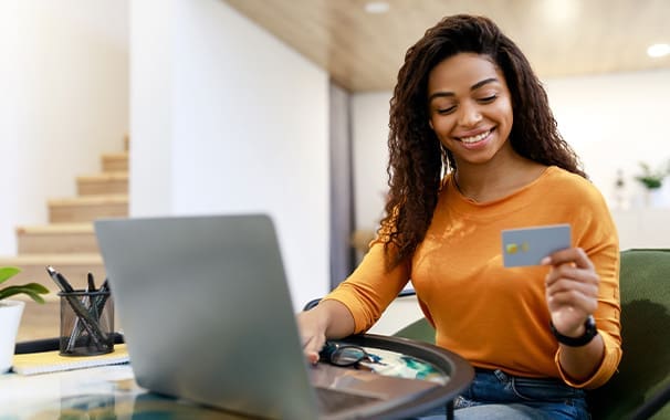 A woman is seated a a laptop and holding a credit card in her hand