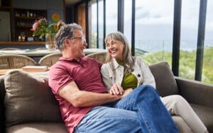 A couple is seated on a sofa and they are looking at each other and smiling